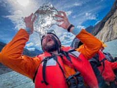 Sean Legnini on a boat in Alaska, holding a piece of glacier ice overhead